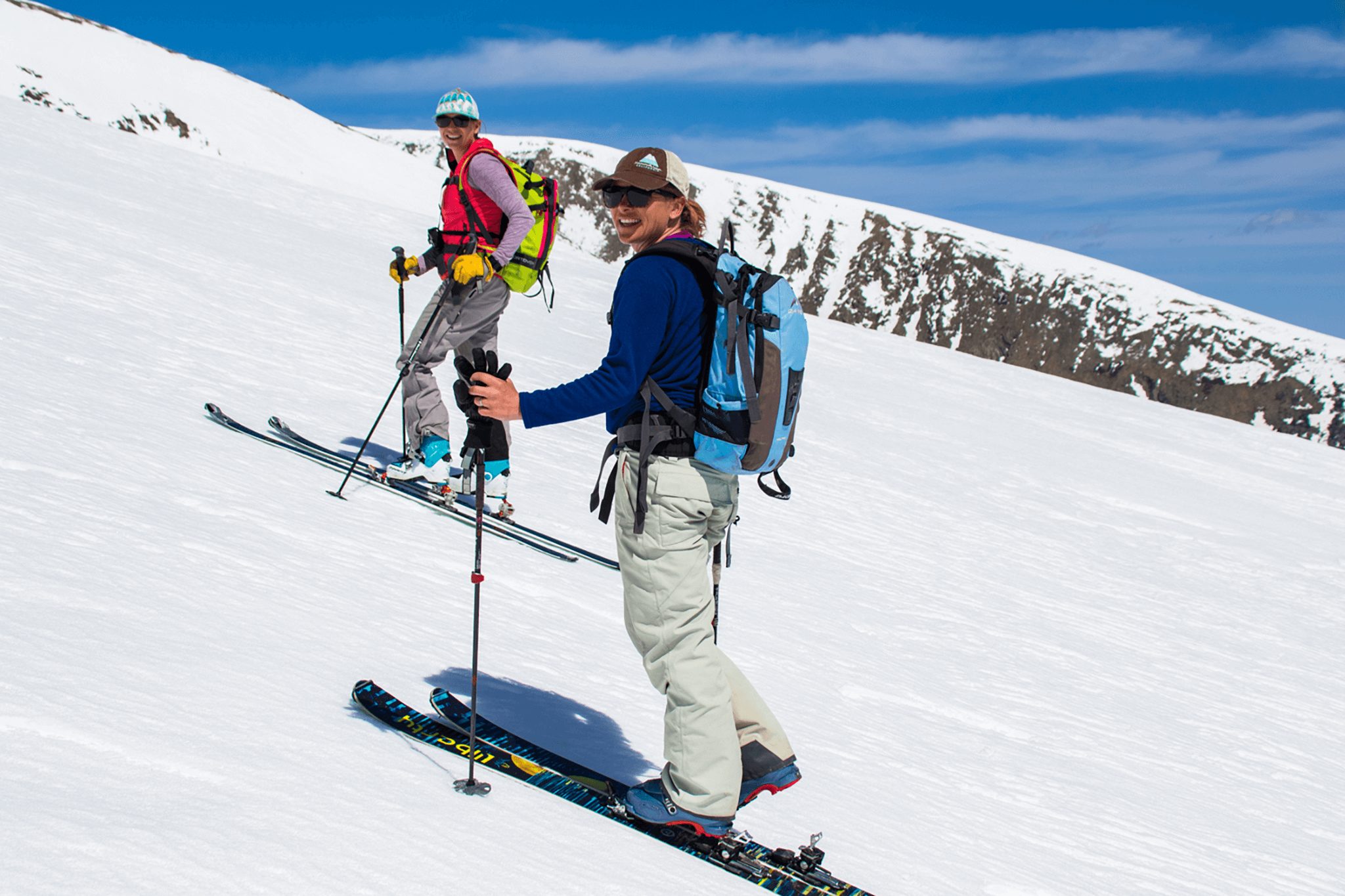 Two backcountry skiers smiling as they skin up a mountain.