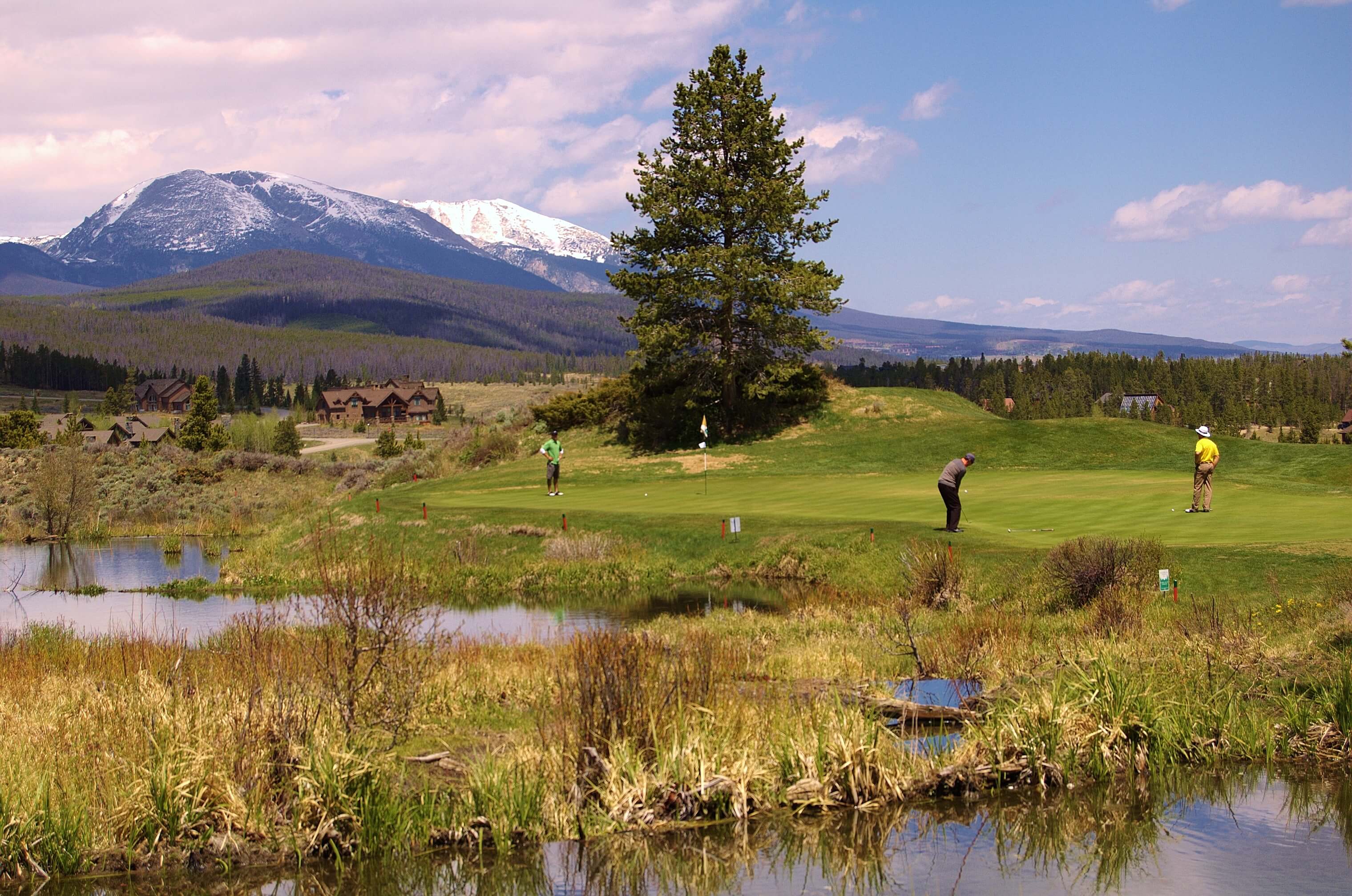 Three men play golf with mountains in background